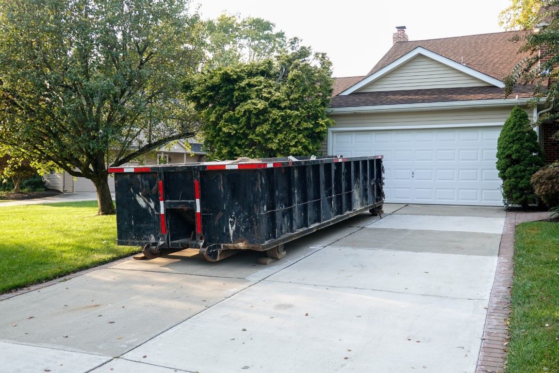 Black roll-off dumpster placed on a wide concrete driveway in front of an attached garage