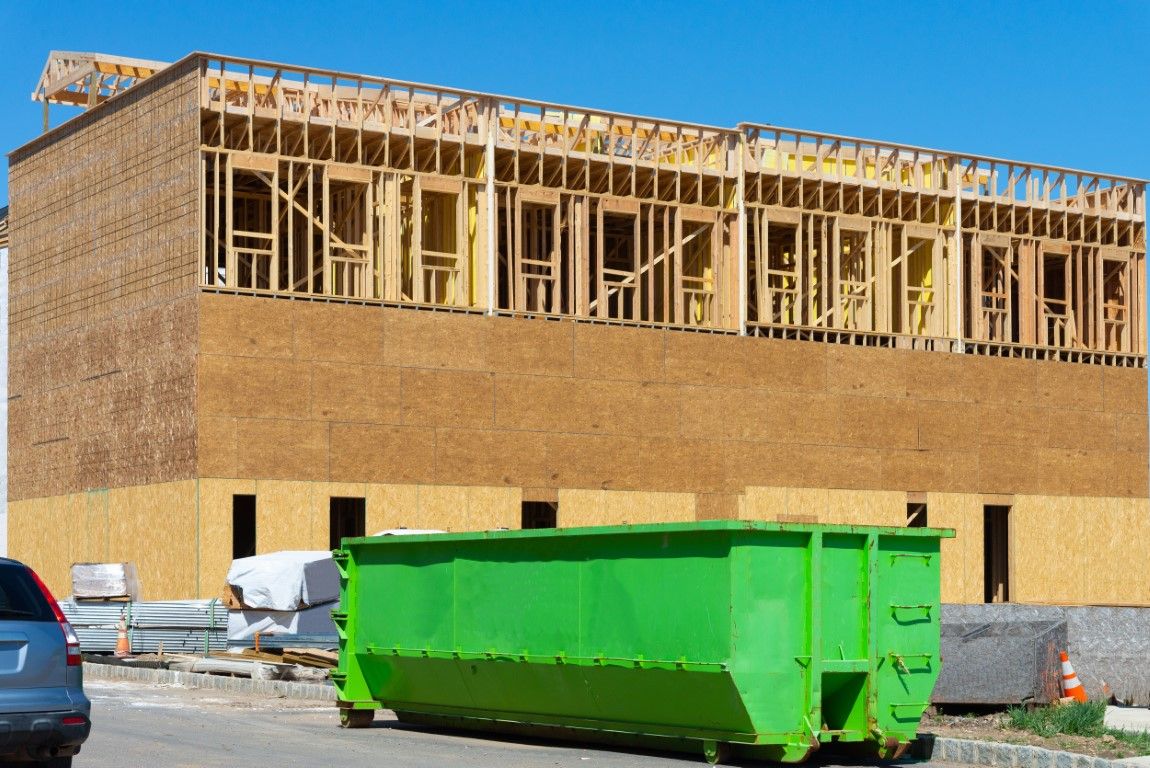 Green roll-off dumpster in front of a two-story house being framed with exposed studs