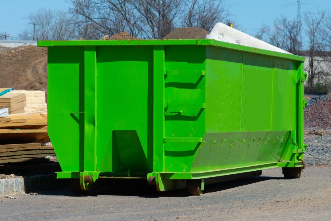 Green roll-off container sitting on packed dirt at a jobsite