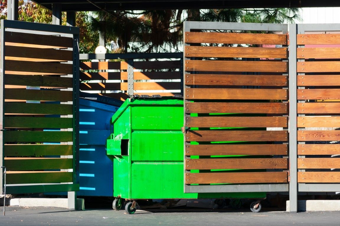 Green dumpster tucked behind a wood-slat enclosure screen