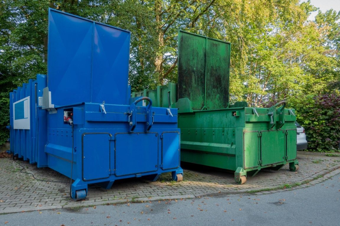 Blue and green dumpster units parked on a paver driveway
