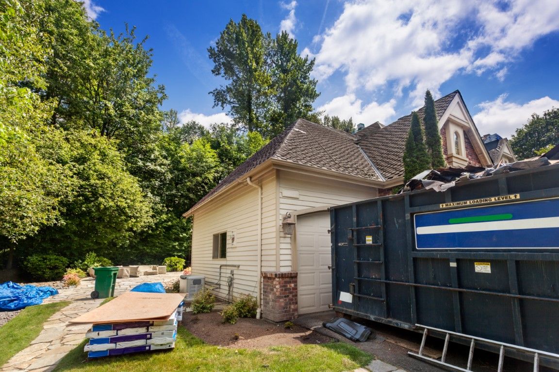 Roll-off dumpster next to a house mid-renovation with building materials stacked nearby