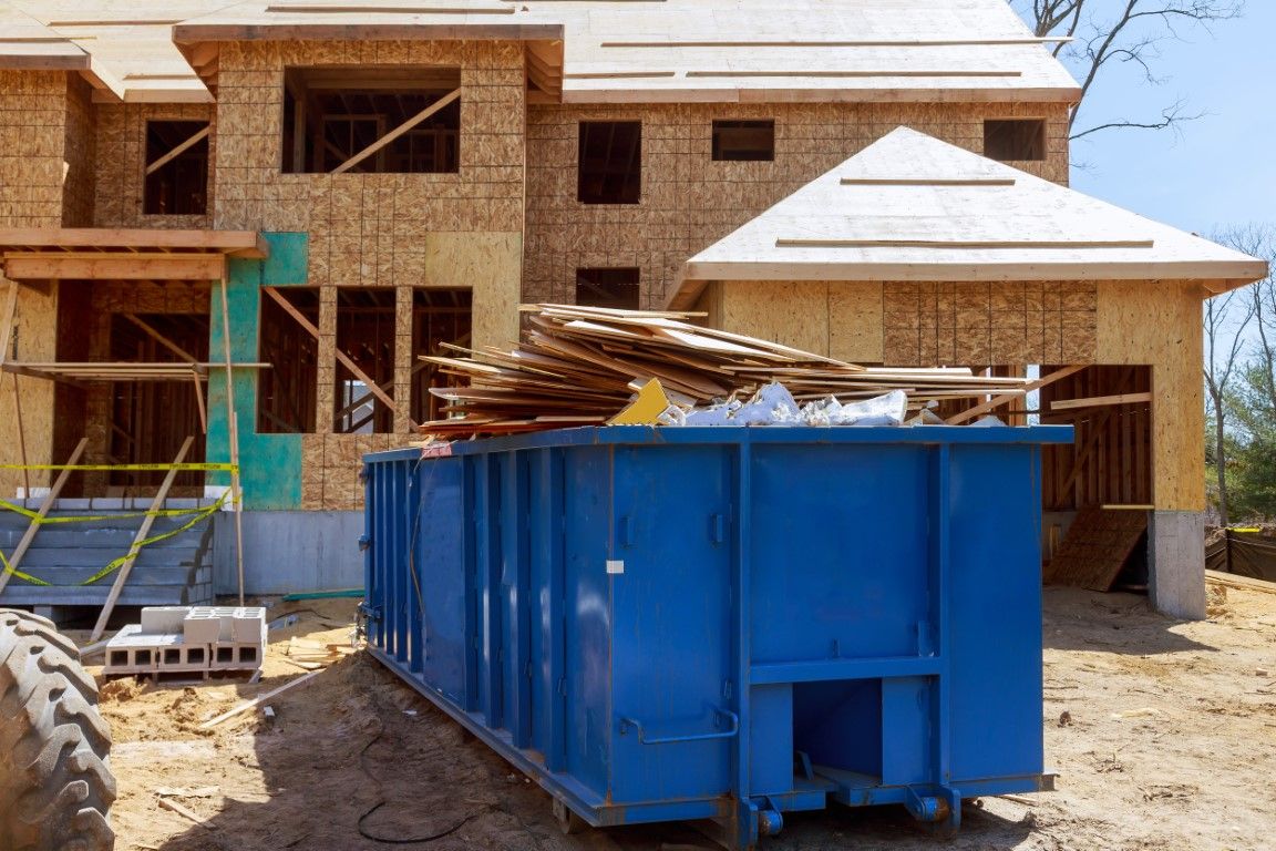 Blue roll-off dumpster loaded with lumber scraps in front of a house under construction