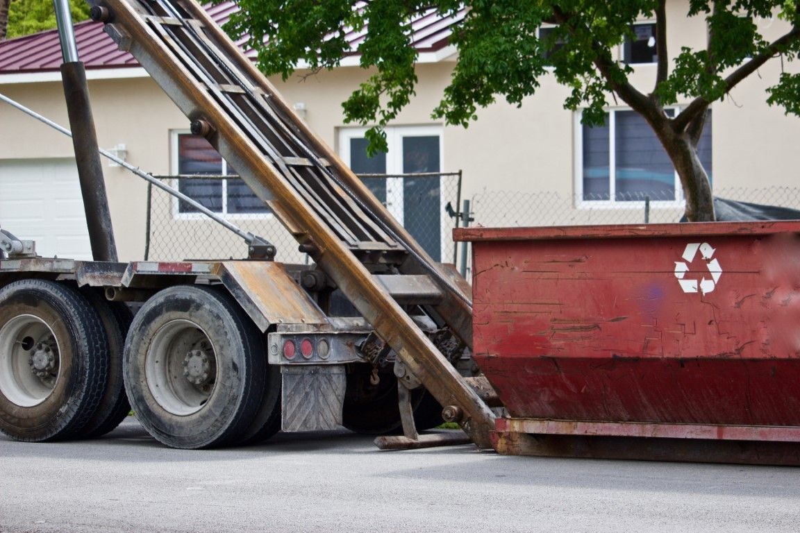 Roll-off truck lowering a red container onto a residential driveway