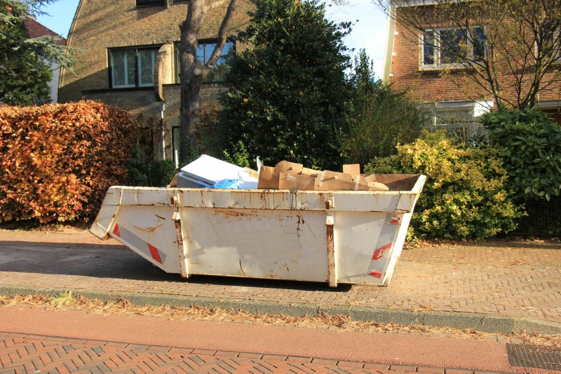 Small open-top dumpster with a few bags of debris parked on a residential driveway