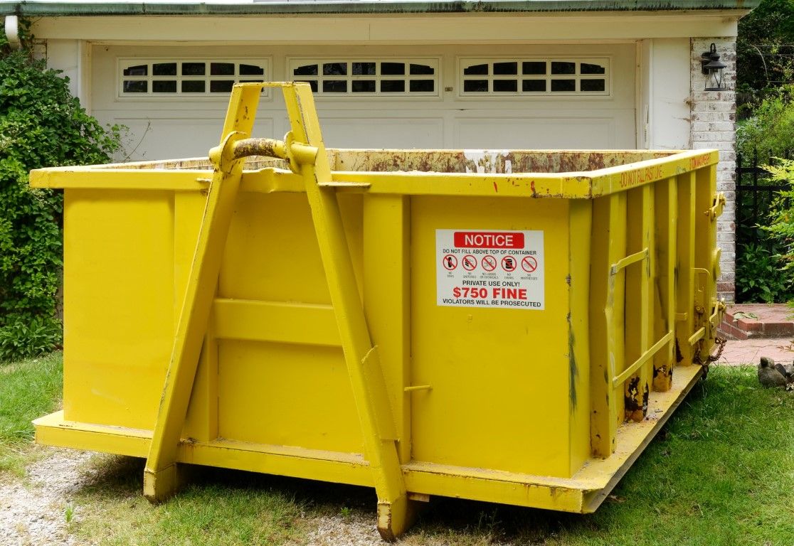 Yellow roll-off dumpster with a hook bar parked in front of a residential garage